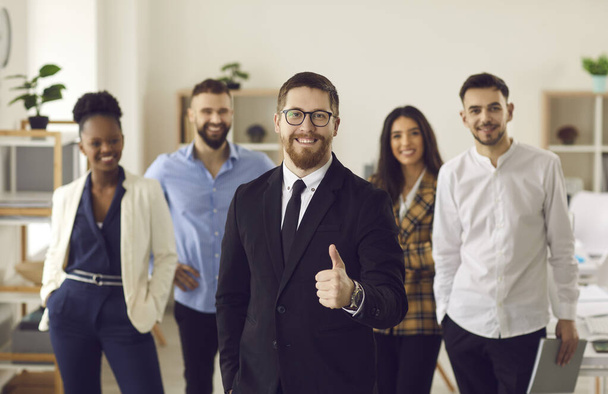 Confident team leader posing in office with diverse colleagues show thumb up - Foto, imagen