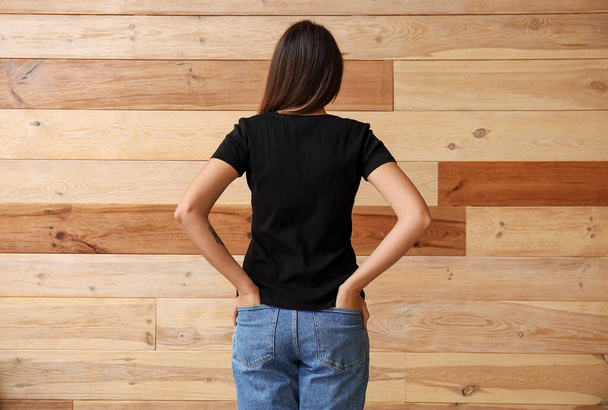 Mujer joven en camiseta en blanco sobre fondo de madera, vista trasera - Foto, imagen