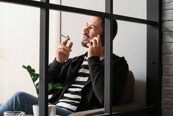 Καπνιστής άντρας που μιλάει στο τηλέφωνο στο σπίτι - Φωτογραφία, εικόνα
