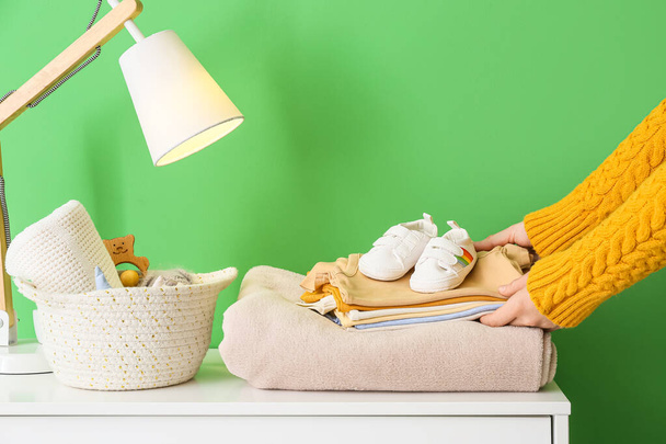 Woman taking baby clothes from chest of drawers near color wall - Foto, imagen