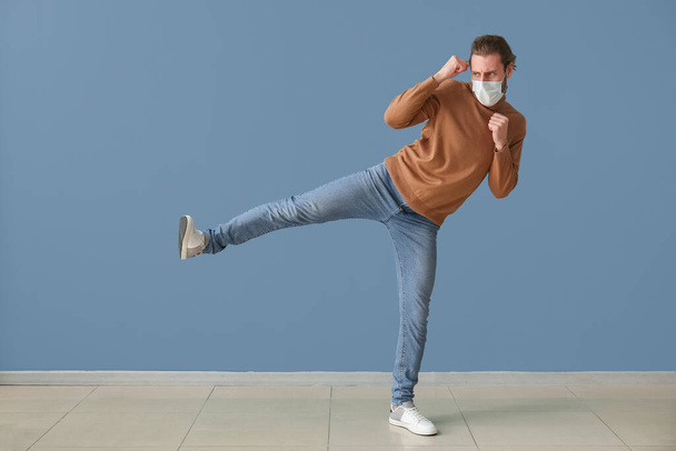 Young male kickboxer wearing medical mask on color background. Concept of strong immunity - Photo, Image