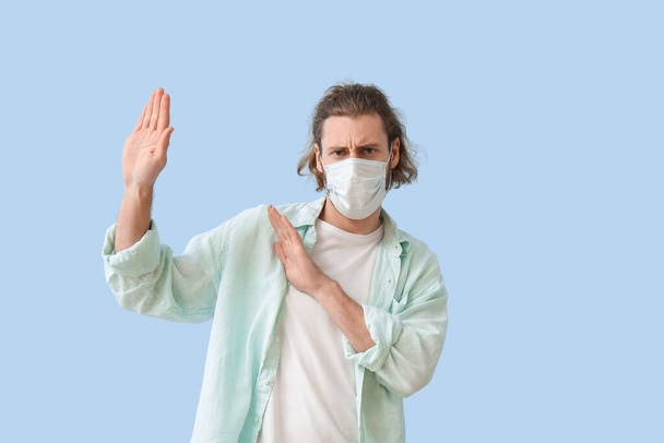 Jongeman met medisch masker vermijden iets op kleur achtergrond - Foto, afbeelding