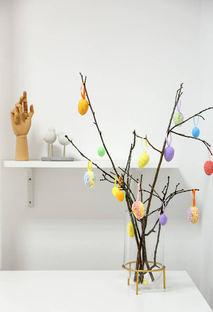 Jarrón con ramas de árbol y diferentes huevos de Pascua en la mesa en la sala de luz - Foto, Imagen