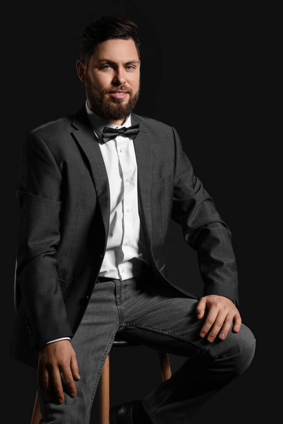 Stílusos szakállas férfi ül széken ellen sötét háttér - Fotó, kép