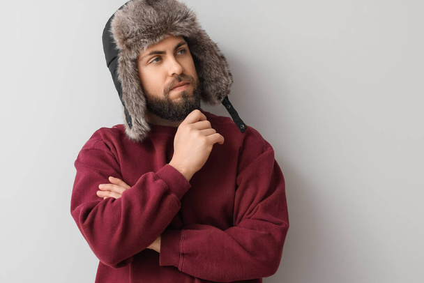 Stílusos szakállas férfi pulóverben és füles kalap könnyű háttér - Fotó, kép