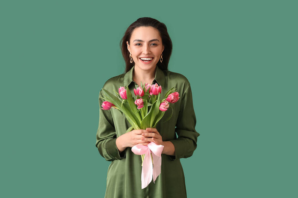 Happy young woman with bouquet of tulips on green background. International Women's Day - Photo, image