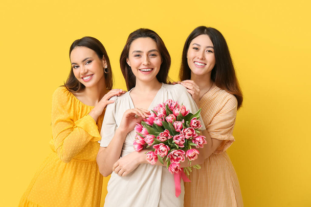 Gyönyörű nők csokor virág sárga háttér. Nemzetközi nőnapi ünneplés - Fotó, kép