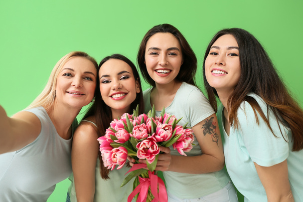 Mooie vrouwen met bloemen nemen selfie op groene achtergrond. Internationale Vrouwendag viering - Foto, afbeelding