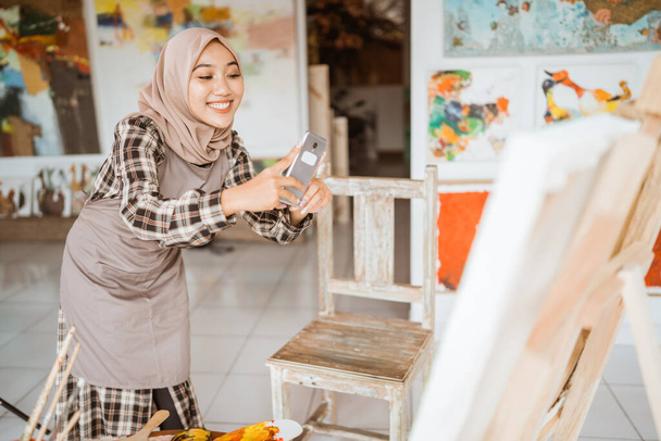 muslim female artist taking picture of her own painting using smartphone - Φωτογραφία, εικόνα