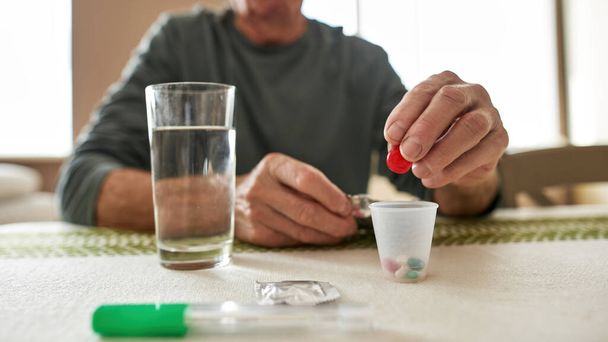 Focus on sick man hand putting pill in plastic cup - Foto, Imagen