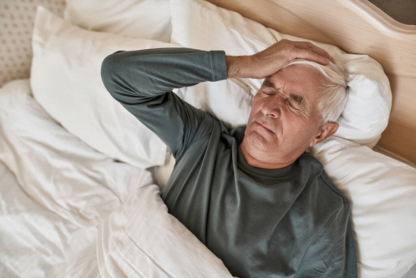 Grey hair man with headache lying on bed at home - Foto, imagen