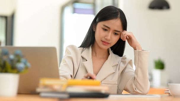 Подчеркнутая азиатская молодая предпринимательница, сосредоточенная и обеспокоенная своим рабочим проектом в офисе. Женское задумчивое мышление, расстроенное собой. - Фото, изображение