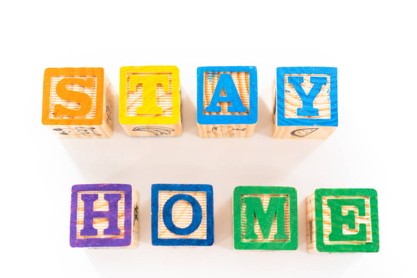STAY HOME uithangbord uit alfabet blokken voor kinderen met zelfgemaakte gezichtsmaskers op een witte achtergrond. - Foto, afbeelding