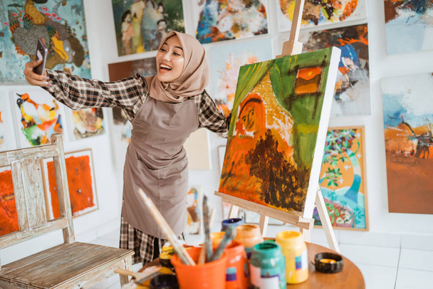 muslim female artist taking selfie picture with her own painting - 写真・画像