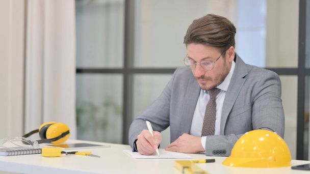 Ingeniero de mediana edad escribiendo en papel en la oficina - Foto, imagen