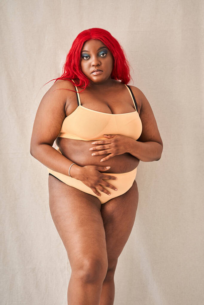 Plus size woman with folds at her body posing at the studio at the beige underwear - Фото, зображення