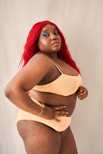 Happy overweight girl with stretch marks holding hands at the waist while posing at camera - Zdjęcie, obraz