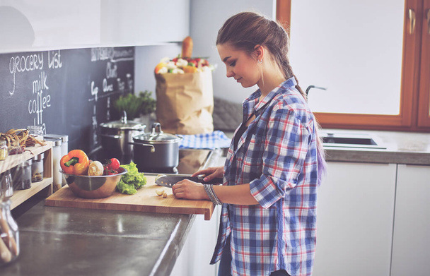 Young woman cutting vegetables in kitchen near desk - 写真・画像