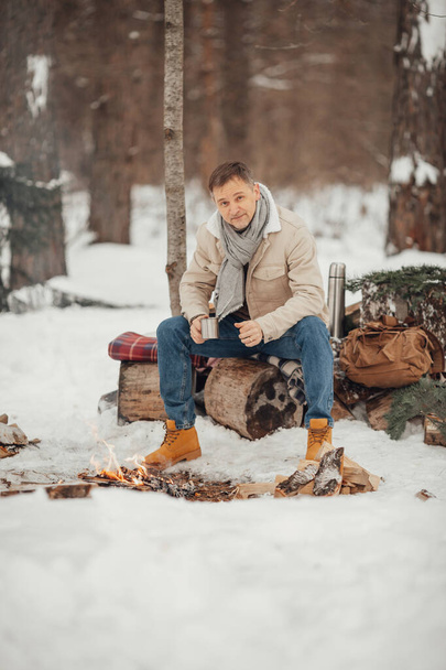 Een man in het winterbos bij het vuur schenkt koffie in. Hoge kwaliteit foto - Foto, afbeelding