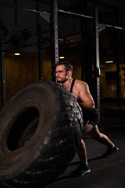 Caucasian man pushing a car tire in the gym.  - Фото, изображение