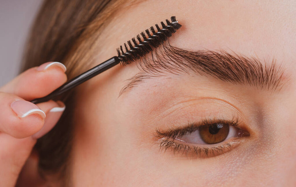 Eyebrow makeup. Woman brushing brows with brows brush closeup. Macro close up of brows. - Photo, image