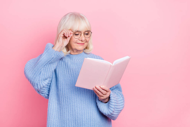 Portrait of attractive cheery focused smart grey-haired woman reading book touching specs isolated over pink pastel color background - Fotó, kép