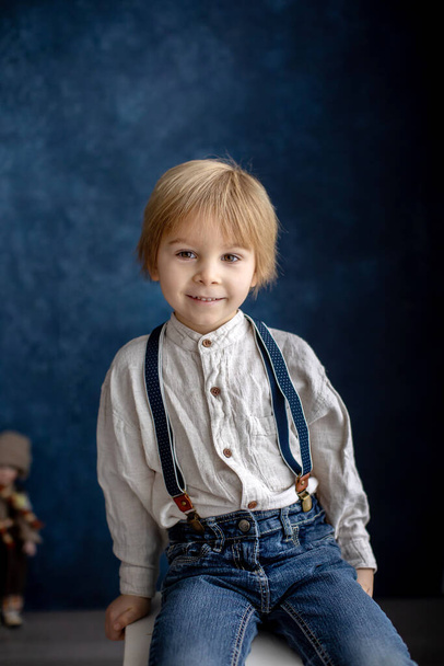 Cute portirait of blond preschool child, boy, on blue background, holding toy - Foto, Bild