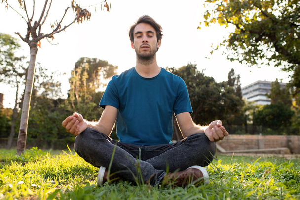 市内の公園で瞑想若い白人男性の正面図。スペースのコピー. - 写真・画像