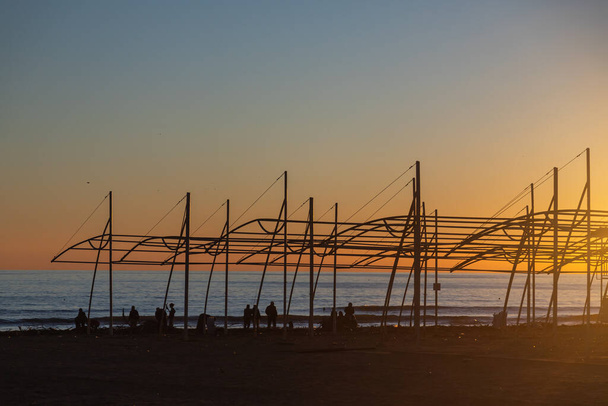 Grupa ludzi sprząta śmieci z plaży i cieszyć się zachodem słońca nad morzem z pięknym horyzontem. Cuda natury. Piękny krajobraz zimowego morza. - Zdjęcie, obraz