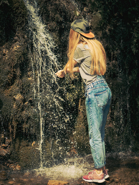 A woman washes her hands in a spring flowing down a rock overgrown with moss. Selective focus - Foto, Bild