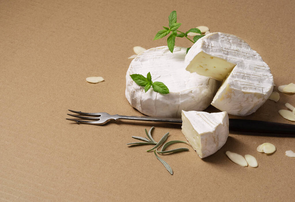 camembert cheese with nuts, fork and rosemary on cardboard. - Photo, image