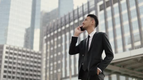 Portrét pohledný podnikatel v černém obleku mluvit do telefonu, zatímco stojí venku na ulici v blízkosti velké kancelářské budovy městské. - Záběry, video