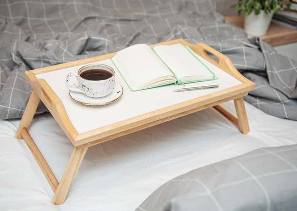 Breakfast in bed. Coffee and notebook on a wooden tray. Work at home concept. - Photo, image