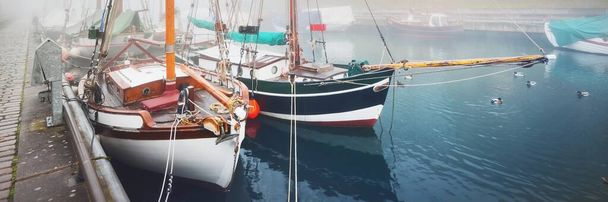 Винтажные деревянные яхты и рыбацкие лодки пришвартованы к пирсу крупным планом. Сильный утренний туман. Германия, Озил, Германия. Спорт, отдых, транспорт - Фото, изображение