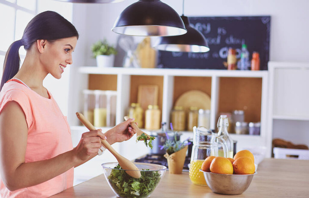Sorrindo jovem mulher misturando salada fresca na cozinha. - Foto, Imagem