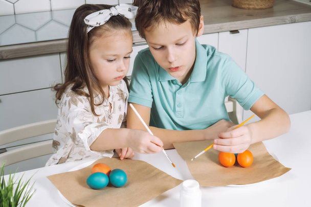 Πορτρέτο ενθουσιώδης χαρούμενη δύο μικρά παιδιά αγόρι και κορίτσι, ζωγραφική χρώμα πινέλο πασχαλινά αυγά. Οικογενειακή παράδοση διακοπών - Φωτογραφία, εικόνα