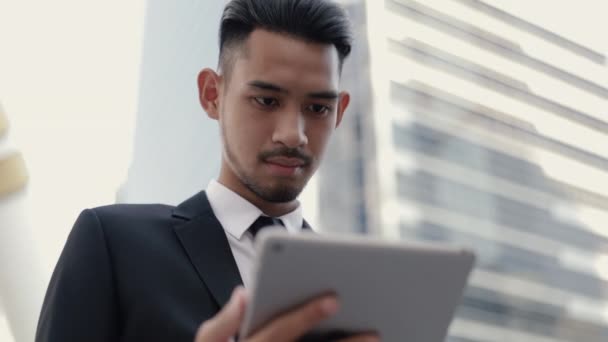 Retrato empresário gerente em um terno preto usando seu tablet de navegação digital financeira, rolagem de mídia social, enquanto está fora na rua perto de um grande edifício de escritórios urbano. - Filmagem, Vídeo