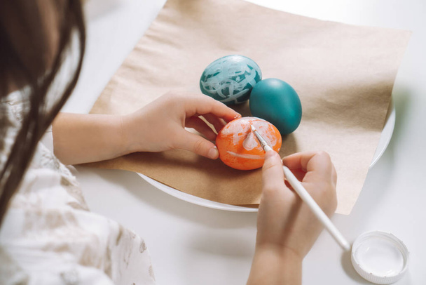 Vágott portré a kislány kezét, festés multi színező húsvéti tyúkok tojás, barna papír lemez asztal, ecset - Fotó, kép