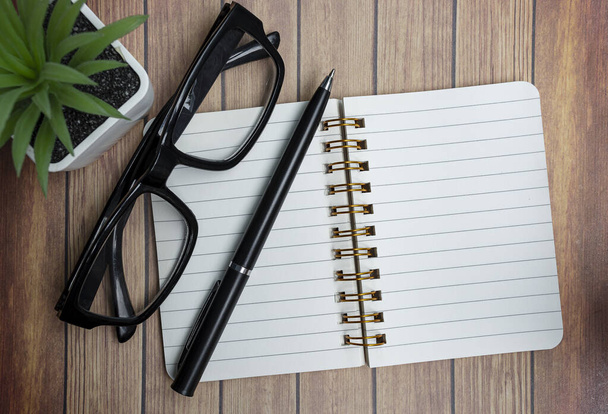 Notepad on wooden desk with potted plant, reading glasses and a pen. Directly above. Flat lay. - Photo, Image