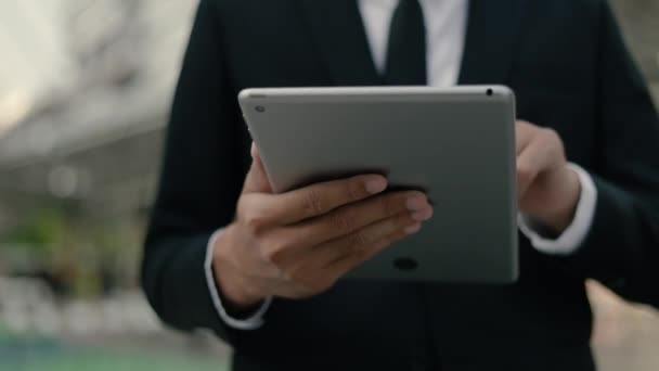 Close-up hand Aziatische zakenman in een zwart pak met behulp van zijn tablet digitaal browsen financiële, scrollen social media feed terwijl staan buiten op straat in de buurt van een groot kantoor gebouw stedelijke. - Video