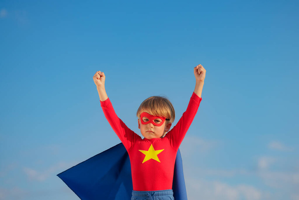Superhero child playing outdoor. Super hero kid against blue summer sky background. Imagination and freedom concept - Photo, image