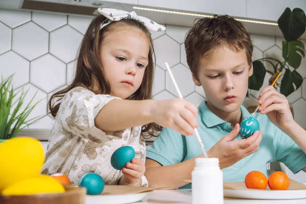 Portrait of concentrated joyful two children, little boy and girl, painting brush multi coloring Easter eggs. Closeup - Φωτογραφία, εικόνα