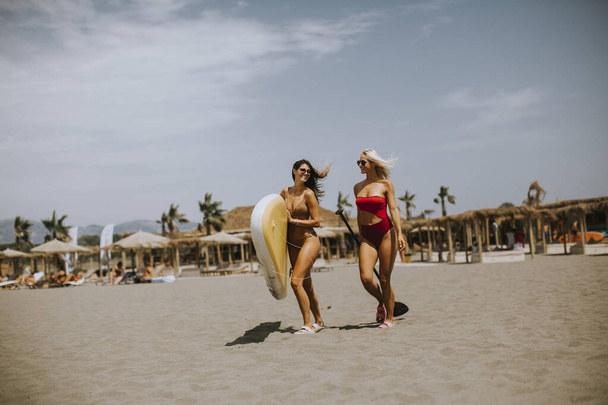 Δύο όμορφες νεαρές γυναίκες με σανίδα στην παραλία μια καλοκαιρινή μέρα - Φωτογραφία, εικόνα