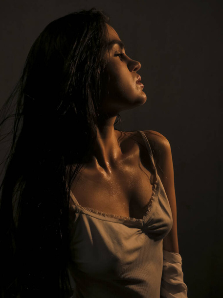 Portret van een donkerharige jonge naakte vrouw met een gladde gebruinde huid in waterdruppels, seksualiteit en schoonheid, esthetiek en gezondheid van het vrouwelijke lichaam - Foto, afbeelding