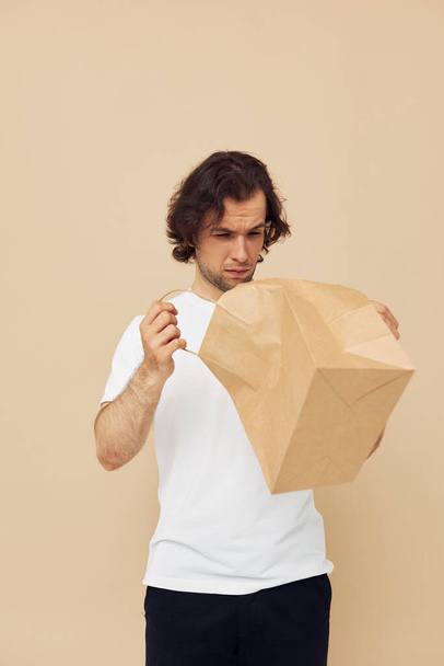 Attractive man in a white T-shirt with paper bag isolated background - Foto, imagen