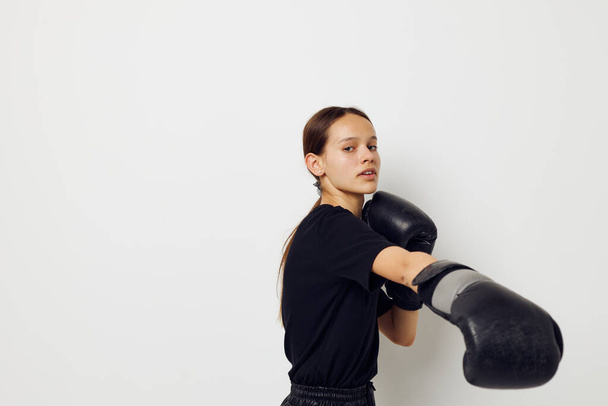 young woman in boxing gloves in black pants and a T-shirt light background - Фото, изображение