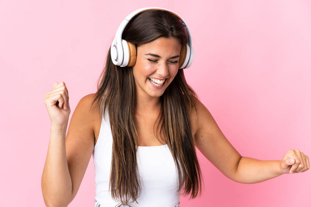 Joven brasileña aislada sobre fondo rosa escuchando música y bailando - Foto, Imagen