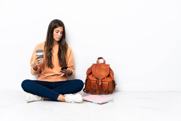 Young student brazilian woman sitting on the floor holding coffee to take away and a mobile - Foto, immagini