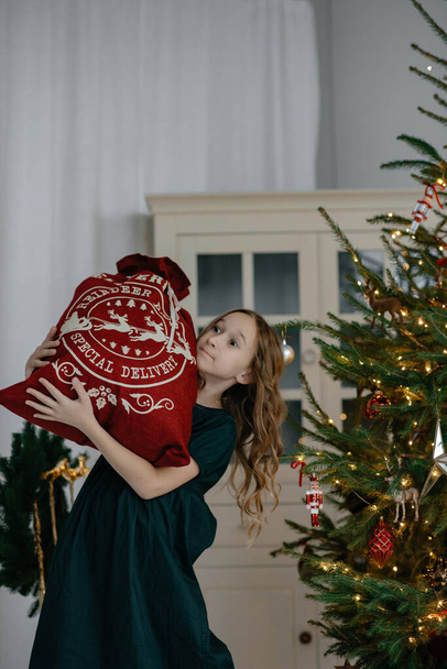 Little girl with a bag of gifts in the hands of a Christmas tree. Photo studio with New Year's decorations. Christmas presents. New Year advertising. Selective focus. The child is on the move. - Zdjęcie, obraz