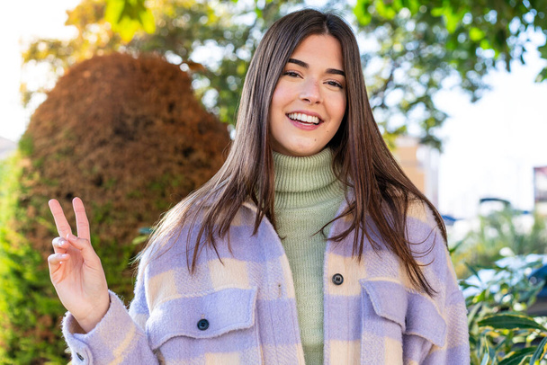 Young Brazilian woman in a park smiling and showing victory sign - Photo, Image